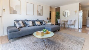 Een woonkamer met een grijze bank, een ronde salontafel en een eethoek met een tafel en stoelen.