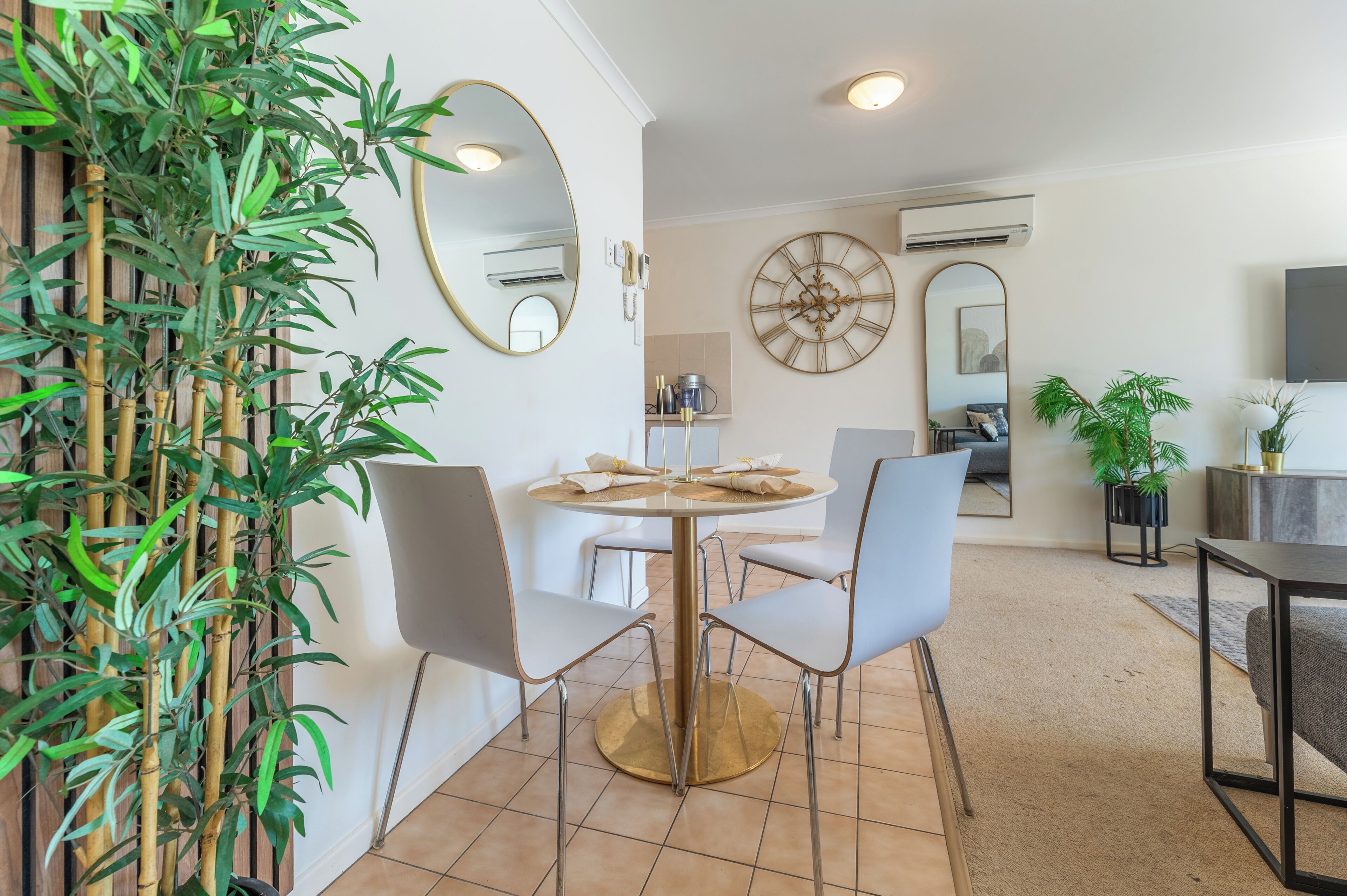 A dining area with a round table, four chairs, a mirror, and a large wall clock.