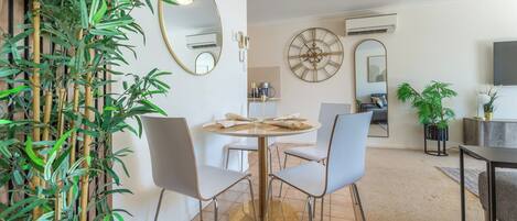 A dining area with a round table, four chairs, a mirror, and a large wall clock.