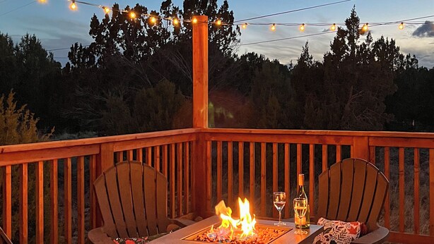 Une terrasse agrémentée d’un foyer, de deux chaises, d’une table et d’une bouteille de vin.