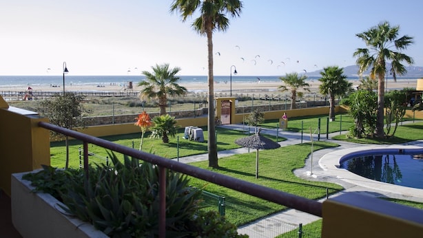Blick vom Balkon auf einen Strand mit Palmen, ein Schwimmbecken und einen Rettungsturm.