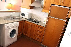 A compact kitchen with a washing machine, microwave, and a refrigerator. - Apartamento Cosmico. (Tarifa)