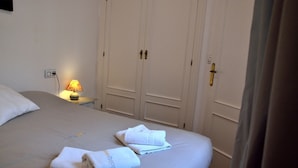 Ein Hotelzimmer mit einem Bett, zwei Handtüchern, einem Nachttisch mit Lampe und einem Schrank mit Türgriff.