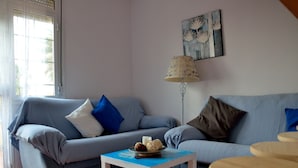 Ein Wohnzimmer mit grauem Sofa, einem kleinen weißen Tisch mit einer Schale, einer Stehlampe und einem Gemälde an der Wand.