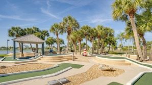 Ein Golfplatz mit einer Laube, Palmen und einem Gewässer im Hintergrund.