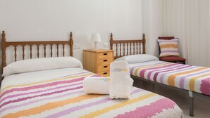 A hotel room with two beds, a wooden nightstand, a lamp, and a striped bedspread. - Puerto Bahía House . (Tarifa)