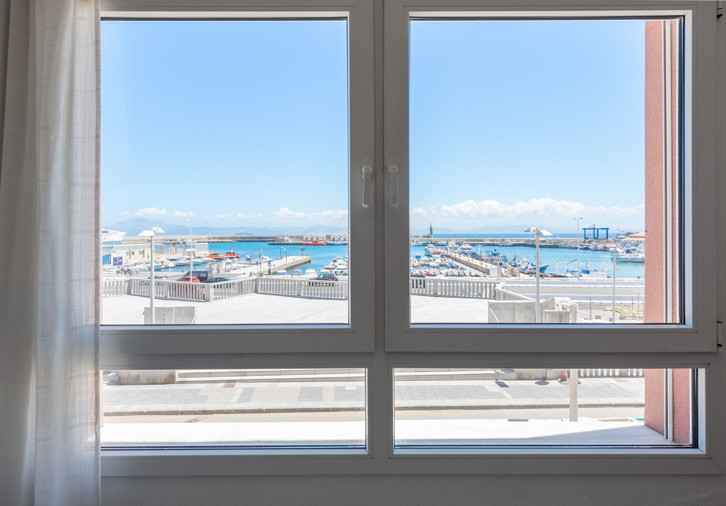 Une fenêtre donnant sur un port de plaisance, des bateaux et un ciel bleu dégagé.