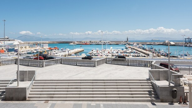 A marina with boats docked, a clear sky, and a view of distant mountains. - Puerto Bahía House . (Tarifa)