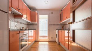A kitchen with orange cabinets, a built-in oven, a washing machine, and a window with a view. - Puerto Bahía House . (Tarifa)