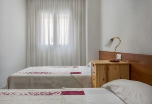 A room with two beds, a wooden nightstand, a desk lamp, and sheer curtains. - Puerto Bahía House . (Tarifa)