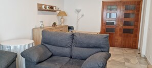 A living room with a grey sofa, a small round table, a wooden cabinet, and a wooden door with glass panels. - Puerto Bahía House . (Tarifa)