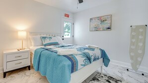 Un dormitorio con cama, mesita de noche, lámpara y un cuadro en la pared.