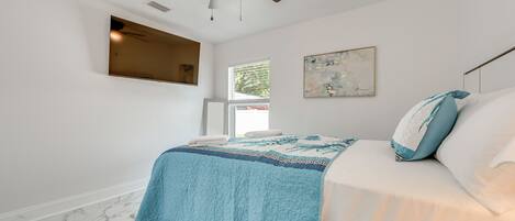 A bedroom with a bed, a ceiling fan, a window, and a painting on the wall.