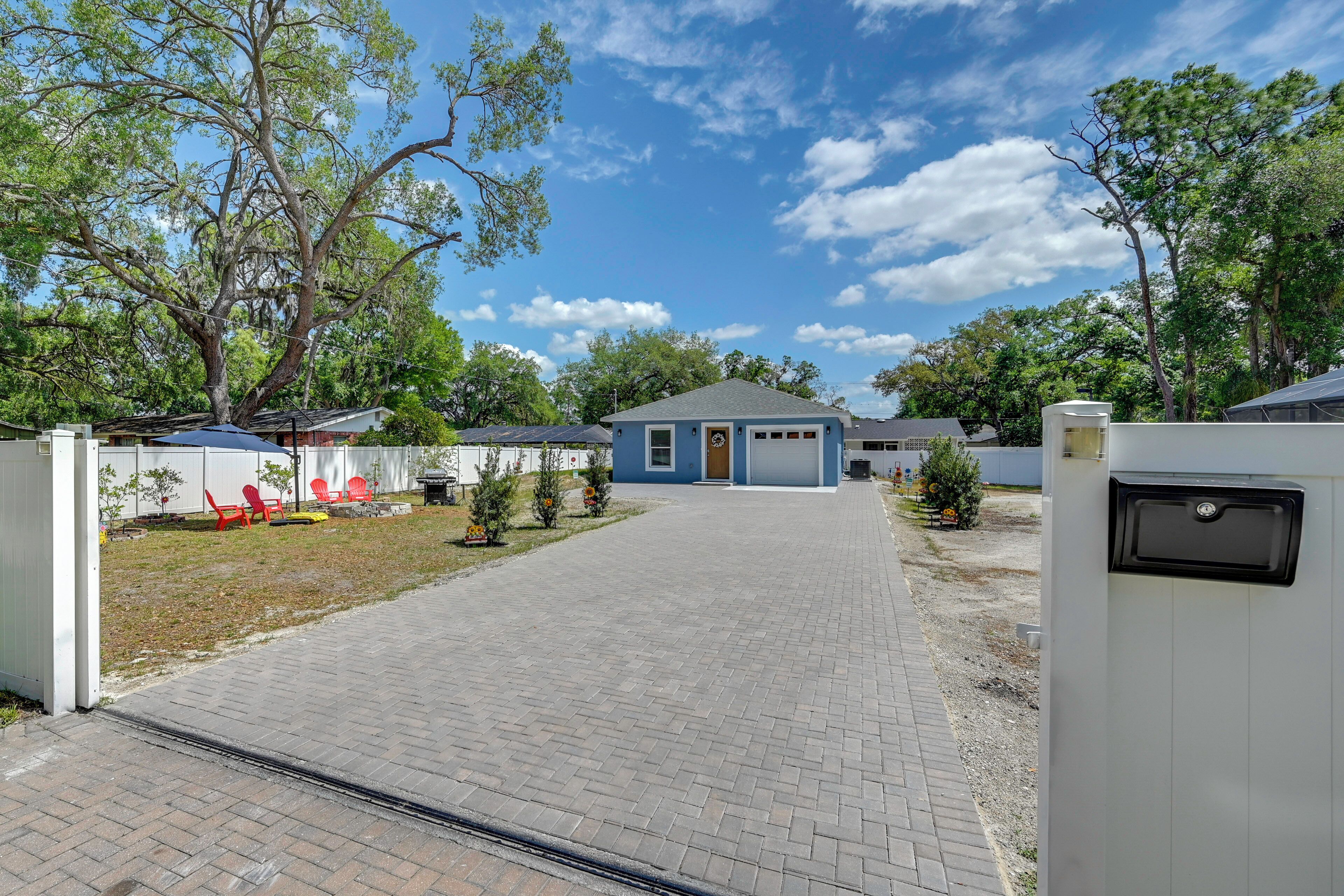 A paved driveway leading to a blue building with a small porch, surrounded by trees and a white fence.