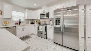 Una cocina moderna con armarios blancos, electrodomésticos de acero inoxidable y suelo de mármol.