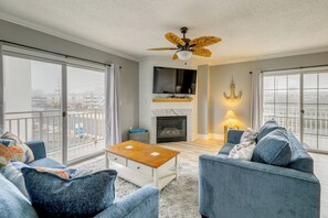 Ein Wohnzimmer mit Kamin, Deckenventilator und Blick durch große Fenster.