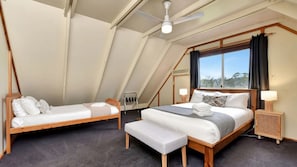 Une chambre avec deux lits, un ventilateur de plafond, une fenêtre avec des rideaux et une petite table de chevet avec une lampe.