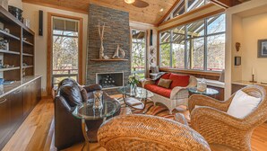 A spacious living area with a fireplace, wicker furniture, and large windows. - Fun w/ Family! Lakefront Gem in Jamestown (Jamestown)