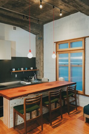 A kitchen with a wooden island, bar stools, hanging pendant lights, and a large window with a view.