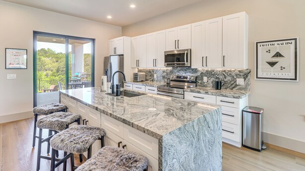 Una cocina moderna con armarios blancos, una isla de mármol y un cubo de basura de acero inoxidable.