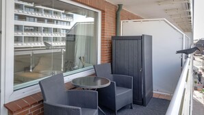 Ein Balkon mit Korbstühlen, einem kleinen runden Tisch und Blick auf ein Gebäude mit Balkonen.
