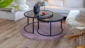 Ein modernes Wohnzimmer mit einem runden Couchtisch, einem weißen Sofa, einem Bücherregal und einem gerahmten Bild an der Wand.