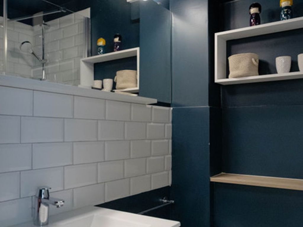 A bathroom with white tiles, a sink, a mirror, and shelves with toiletries.