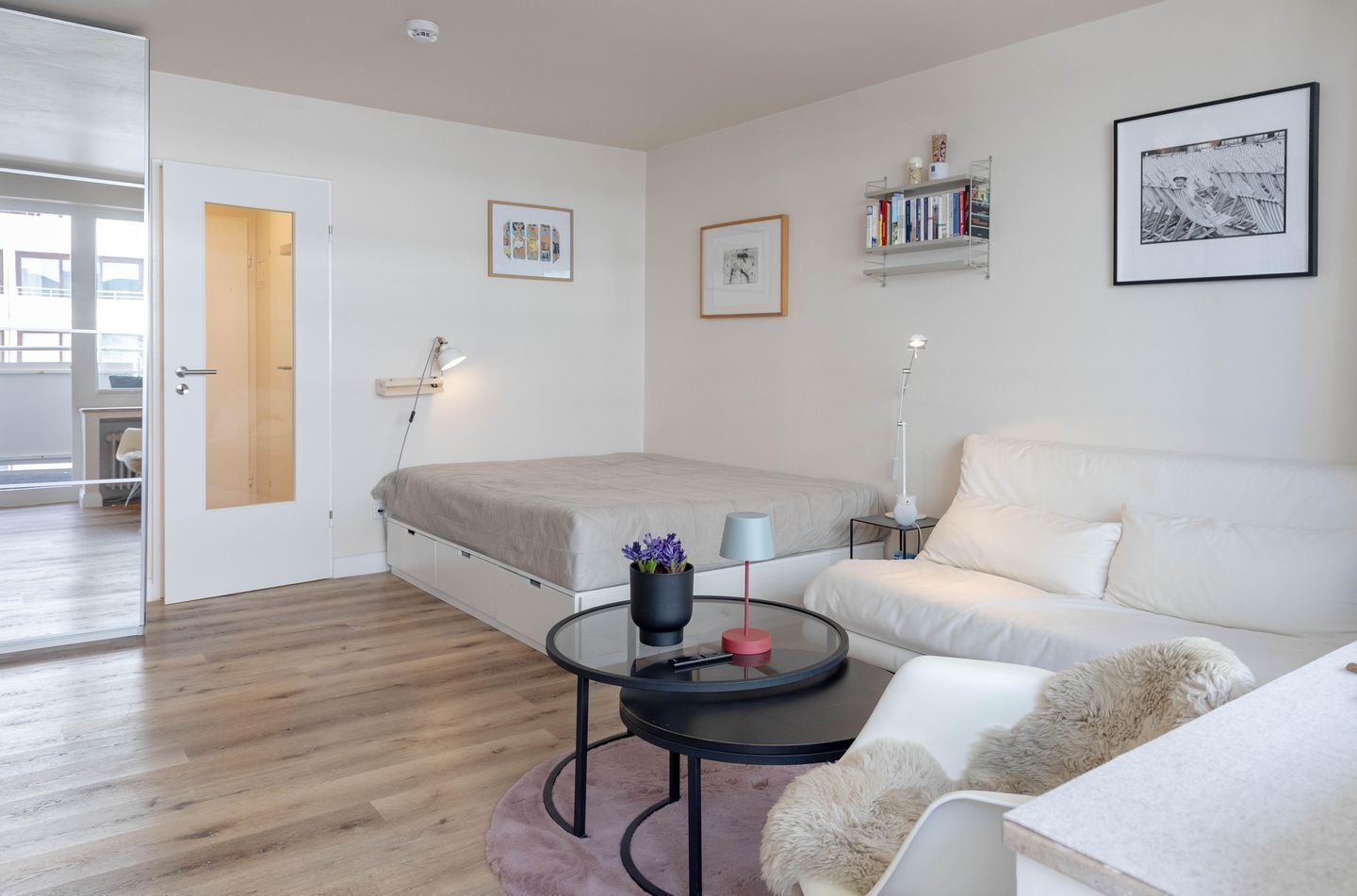 A modern bedroom with a bed, a white sofa, a round coffee table, and a bookshelf.