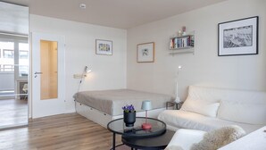 Ein modernes Schlafzimmer mit einem Bett, einem weißen Sofa, einem runden Couchtisch und einem Bücherregal.