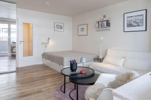 A modern bedroom with a bed, a white sofa, a round coffee table, and a bookshelf. - WOMEN'S ROOM - Suite No. 7 - Women's room - Suite No. 7 (Sylt)