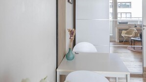 Ein modernes Wohnzimmer mit einem weißen Tisch, einer Uhr, einer Vase mit Blumen und einer Schiebetür zu einem anderen Raum.