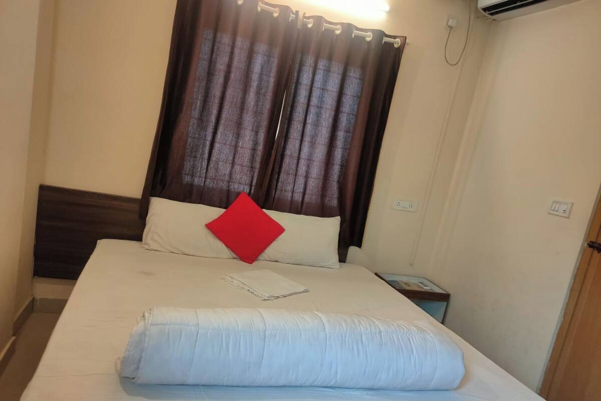 A hotel room with a bed, curtains, a nightstand, and a wall socket.