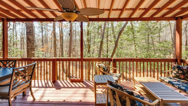 Eine Holzterrasse mit Deckenventilator, Gartenmöbeln und Blick auf einen Wald.