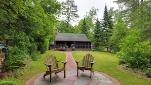 Ein Haus mit Veranda, zwei Adirondack-Stühlen und einem Steinweg, der zum Eingang führt.
