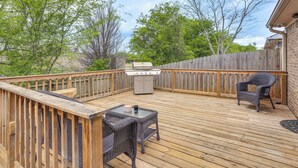 Un patio in legno con barbecue, mobili in vimini e vista sugli alberi.