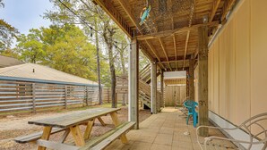 A covered picnic area with wooden benches and picnic tables, a wooden fence, and a wooden building in the background. - Deck & Games! Pet-Friendly Oak Island Home (Oak Island)