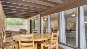 An outdoor patio with a round wooden table and chairs, a brick wall, and large sliding glass doors leading to an interior space. - Saguaro Retreat! Extended Stay in Tucson (Tucson)