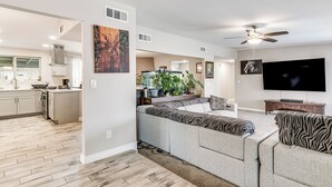 A modern living room with a sofa, a flat-screen TV, and a ceiling fan. - Saguaro Retreat! Extended Stay in Tucson (Tucson)