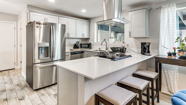 A modern kitchen with stainless steel appliances, a central island, bar stools, and a window with curtains. - Saguaro Retreat! Extended Stay in Tucson (Tucson)