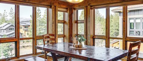 Une table de salle à manger en bois, avec des bancs, de grandes fenêtres et un lustre.
