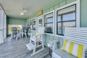 Eine überdachte Veranda mit weißer Möbel, einem Deckenventilator und Blick auf die Stadtlandschaft durch große Fenster.