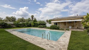 Una piscina rectangular amb vores de pedra, envoltada per un jardí ben cuidat i arbustos diversos.