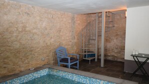 A stone-walled room with a small pool, a chair, and a metal spiral staircase. - Villa in Chiaramonte Gulfi with 3 bedrooms sleeps 8 (Chiaramonte Gulfi)