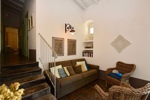 Una sala de estar con un sofá, una silla de mimbre, una escalera y una estantería.