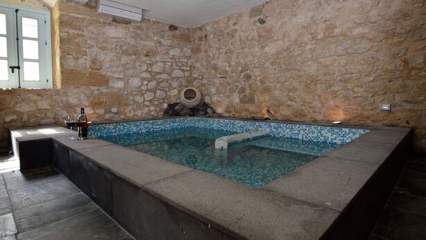 A stone-walled room with a tiled pool, a stone bench, and a small table with a bottle and glasses. - Villa in Chiaramonte Gulfi with 3 bedrooms sleeps 8 (Chiaramonte Gulfi)