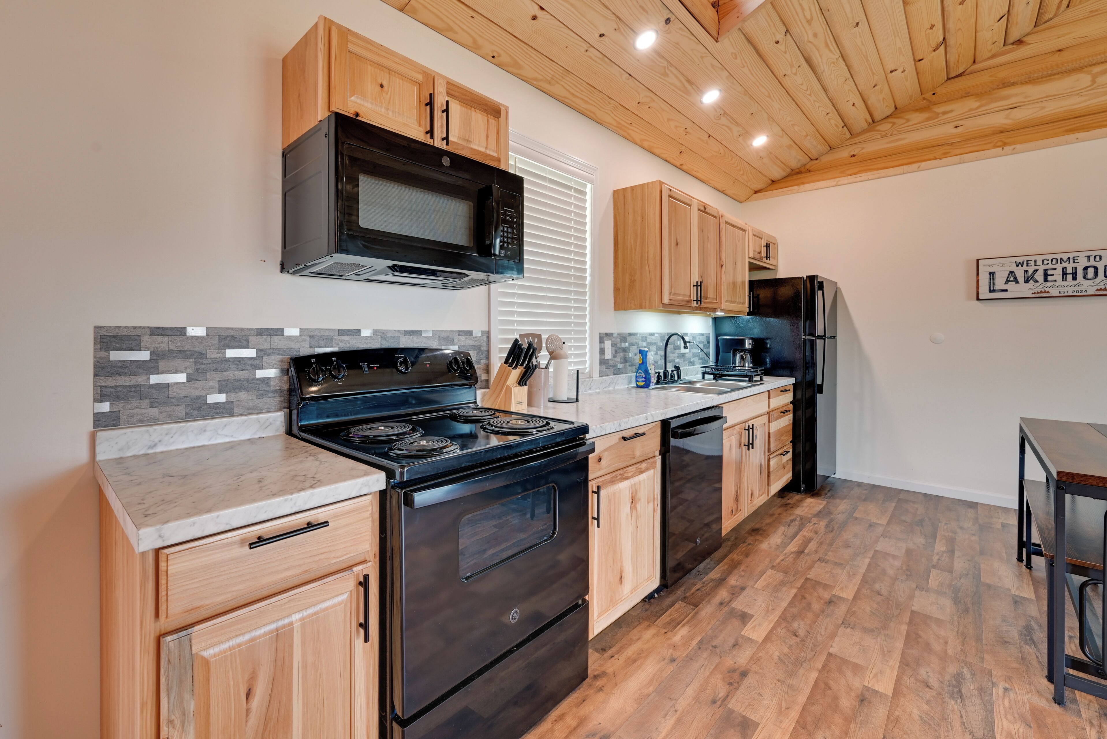 Une cuisine avec des meubles de rangement en bois, une cuisinière noire, un four à micro-ondes et un réfrigérateur.