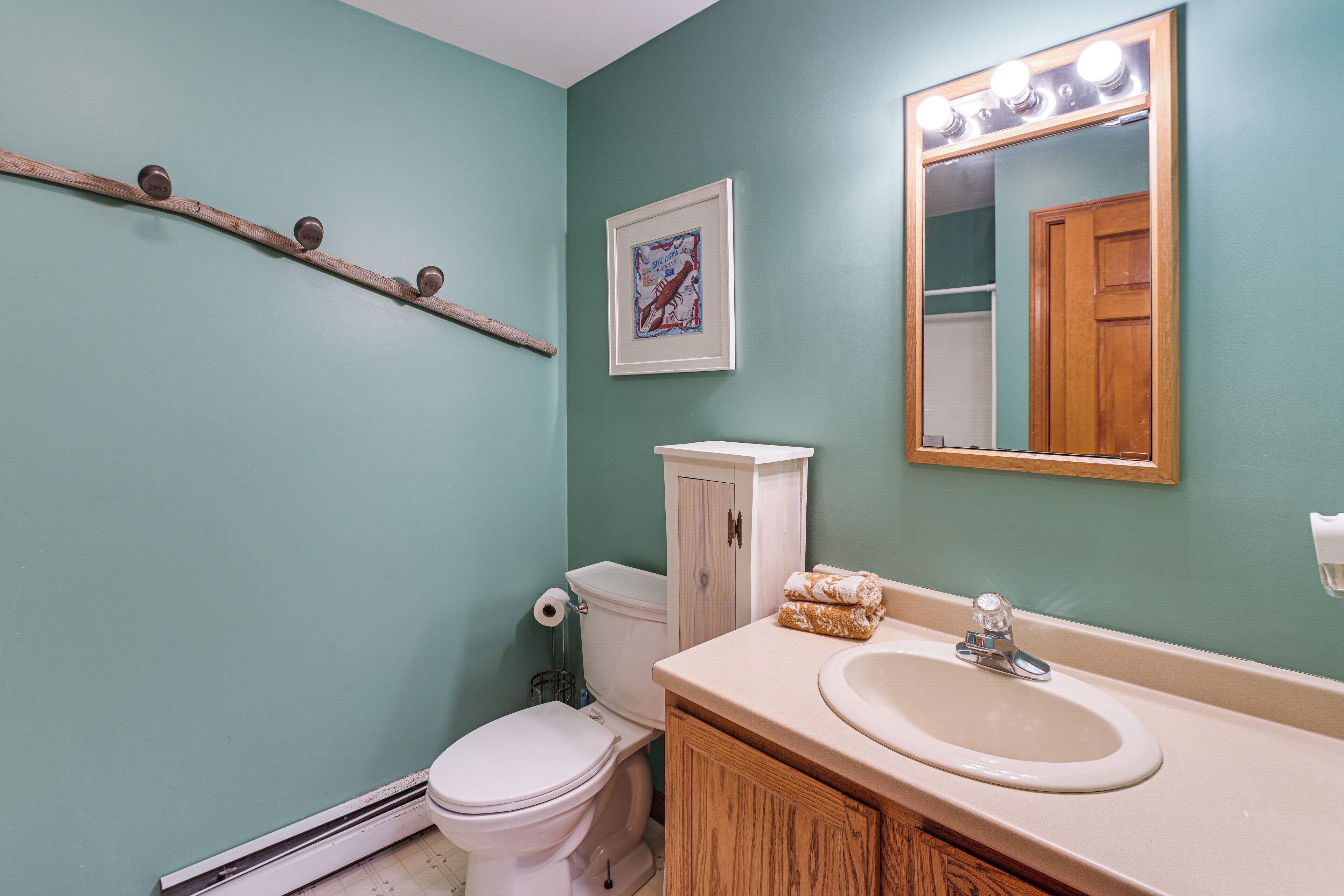 A bathroom with a toilet, sink, mirror, and a wooden shelf.