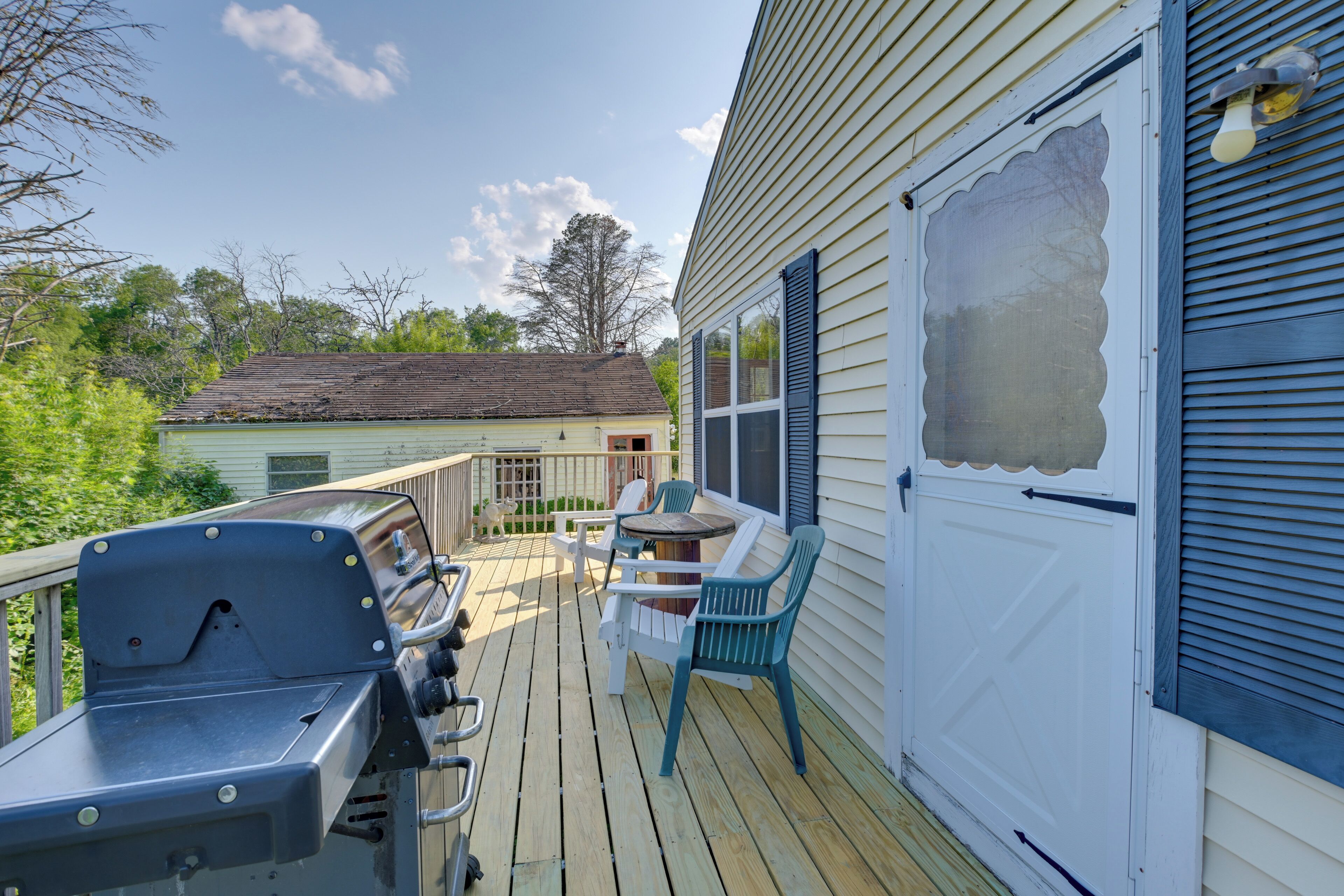A deck with outdoor furniture and a grill, overlooking a house with a green roof.