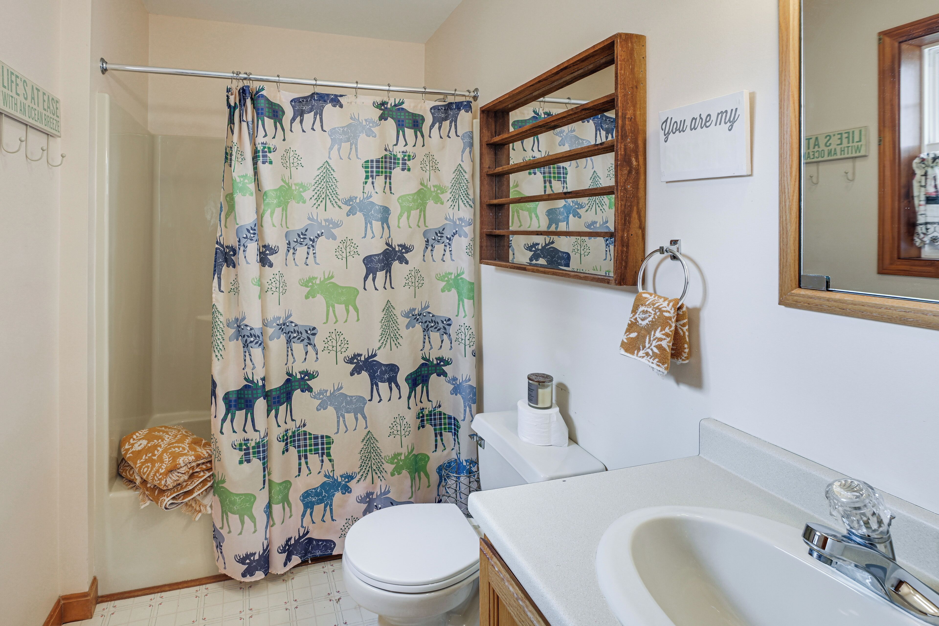 Un baño con cortina de ducha estampada con motivos animales, un inodoro, un lavamanos con espejo y un perchero para toallas.