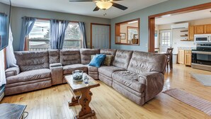 A living room with a sectional sofa, a ceiling fan, and a view to the kitchen. - 9-Acre Riverfront Home in Milbridge w/ Deck & Yard (Milbridge)